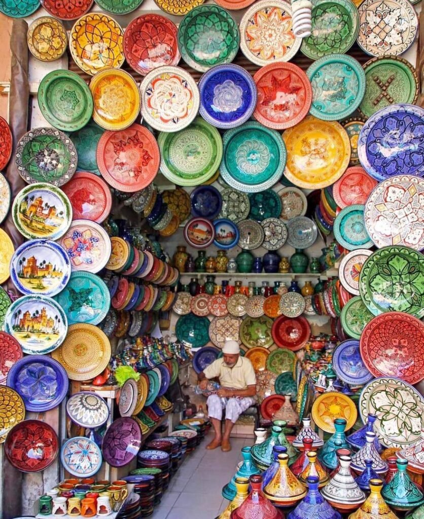 A vendor sits inside a crowded shop surrounded by colorful hand-painted ceramic plates and tagine pots.