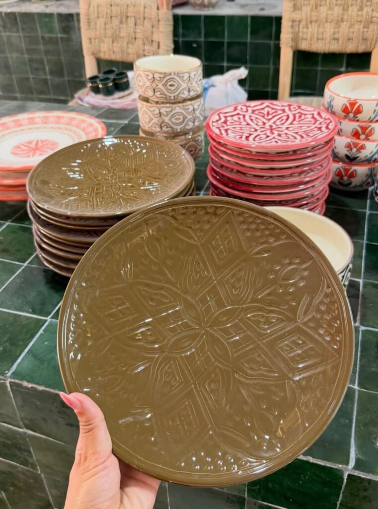 Hand holding a brown embossed ceramic plate before stacks of patterned plates and bowls.